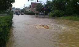 Überflutete Straße ist zu sehen, Wasser fließt in einen Kanal. Hier muss der Hochwasserschutz verbessert werden.
